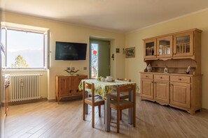 A dining area with a table and chairs, a television, wooden cabinets, and a window with a view.