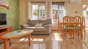 A living room with a sofa, TV, glass table, and wooden chairs. - Holiday Apartment "Vivienda Con Piscina" with Private Pool, 3 Terraces & Wi-Fi (Nerja)