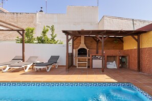 Una piscina con sillones de descanso, zona de barbacoa y un área de estar cubierta.