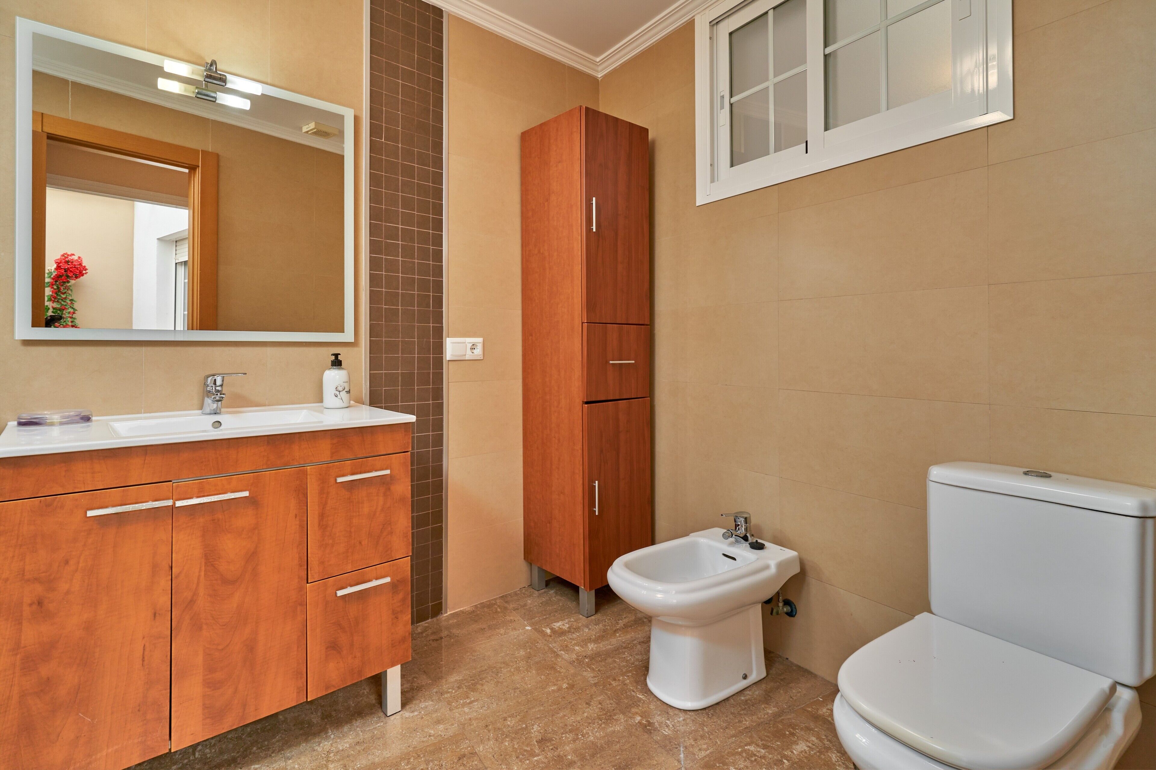 A bathroom with a white sink, wooden cabinets, a bidet, and a toilet.