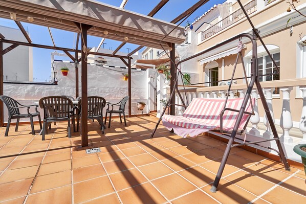 Un espace extérieur abrité, équipé d’une balançoire, de chaises et d’une table.