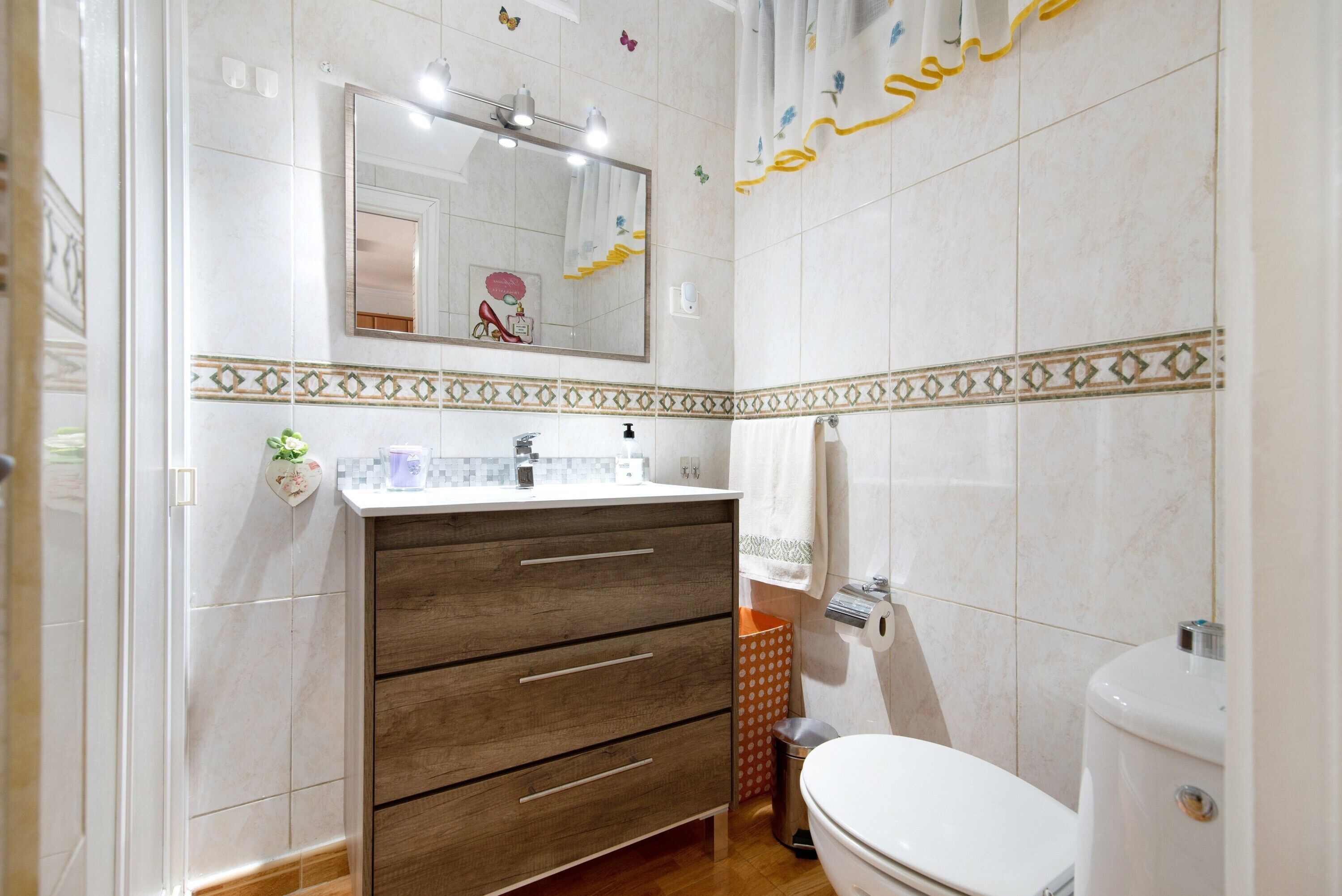 Ein Badezimmer mit einem Holzkosmetikschrank, einer Toilette und einem Spiegel über dem Waschbecken.