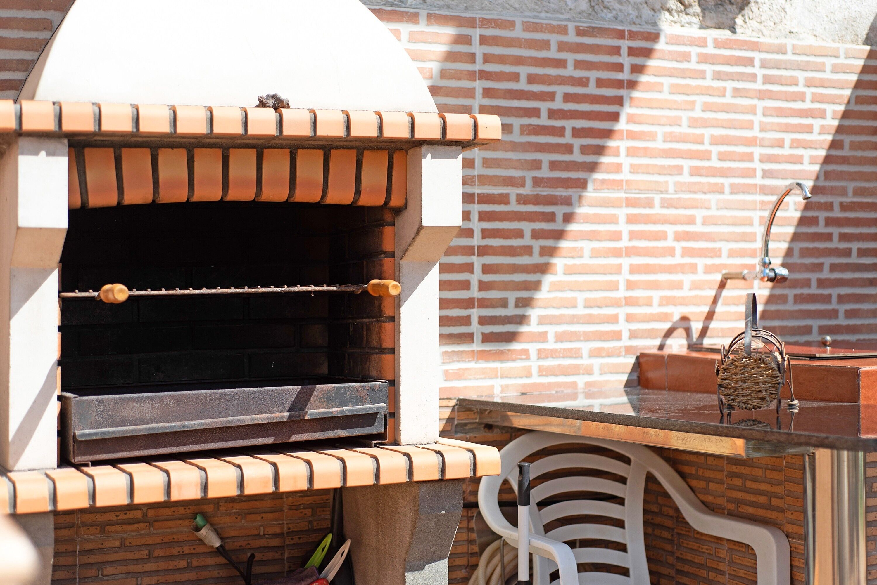 Forno in mattoni all'aperto con canna fumaria, lavello in metallo e sedia in plastica bianca.