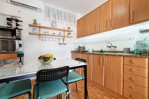 Una cocina con armarios de madera, microondas, una mesa de vidrio y un cuenco de fruta.