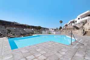 Une piscine avec une terrasse carrelée, un mur en pierre et un escalier menant à un bâtiment blanc doté de balcons.