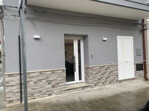 Um edifício residencial com fachada cinza, parte inferior revestida de azulejos, porta de correr de vidro e porta branca.