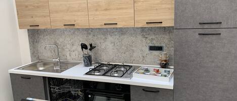 A compact kitchen with wooden upper cabinets, a white countertop, a stainless steel sink, a gas stove, and a dishwasher.