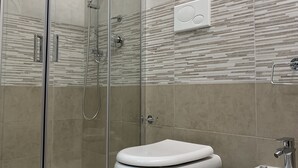 Ein Badezimmer mit Duschkabine, zwei Toiletten und einem Bidet.