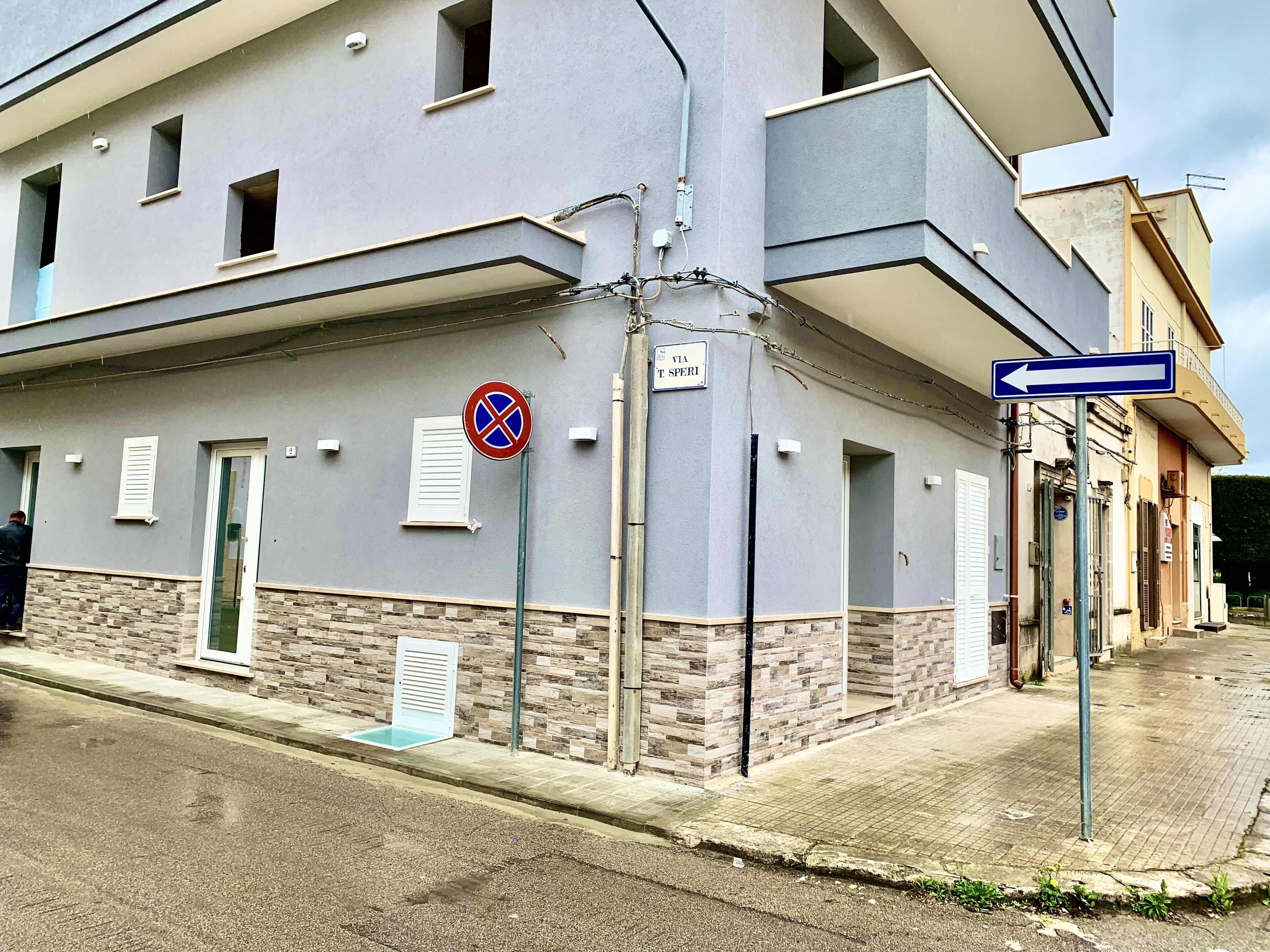 A building with a grey facade, a no parking sign, and a directional sign pointing left.
