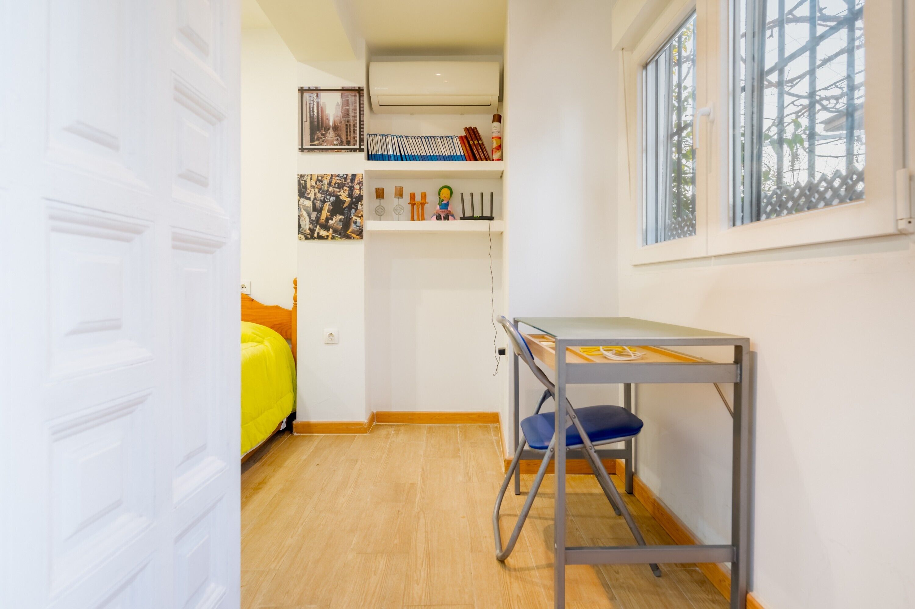 A compact room with a bed, a desk, and shelves with various items.
