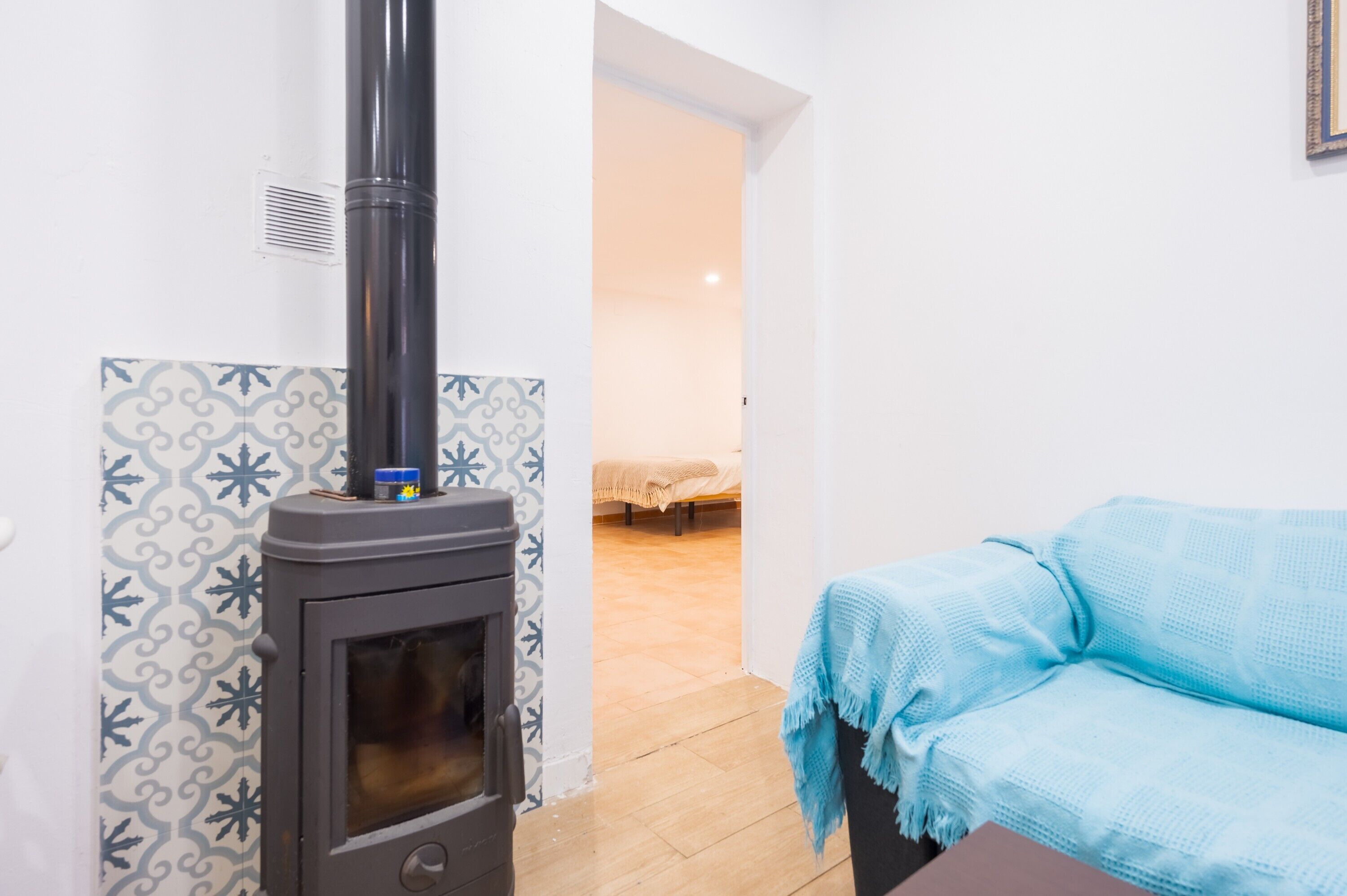 A room with a wood-burning stove, a patterned wall, a bed, and a blue blanket on a sofa.
