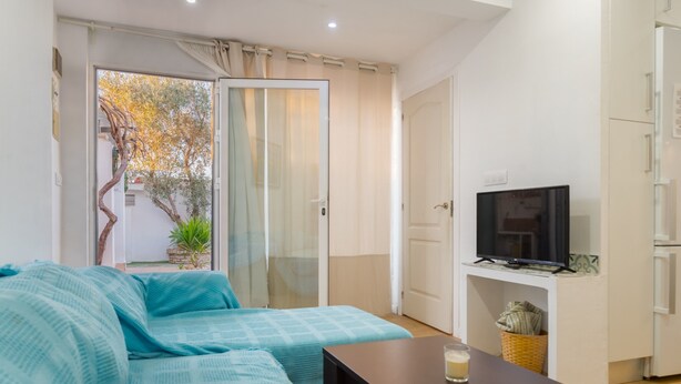 A modern living room with a sofa, a television on a stand, and a glass door leading to a balcony. - Holiday Home with Private Pool and A/C near Seville (La Rinconada)