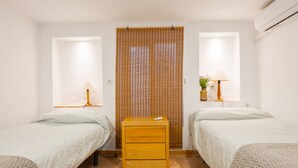 A room with two beds, a small wooden nightstand, a window with blinds, and a wall-mounted air conditioner. - Holiday Home with Private Pool and A/C near Seville (La Rinconada)