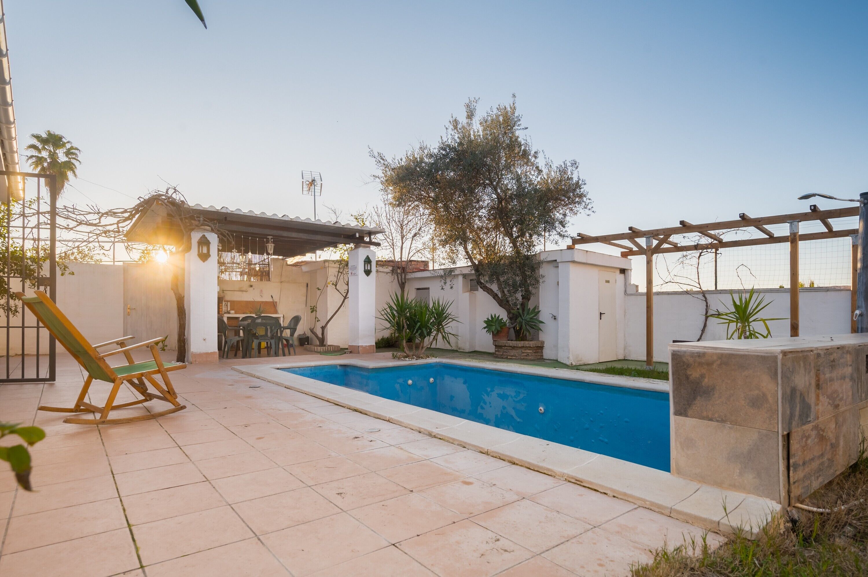 Una piscina con pérgola, una mecedora y un patio con mesa y sillas.