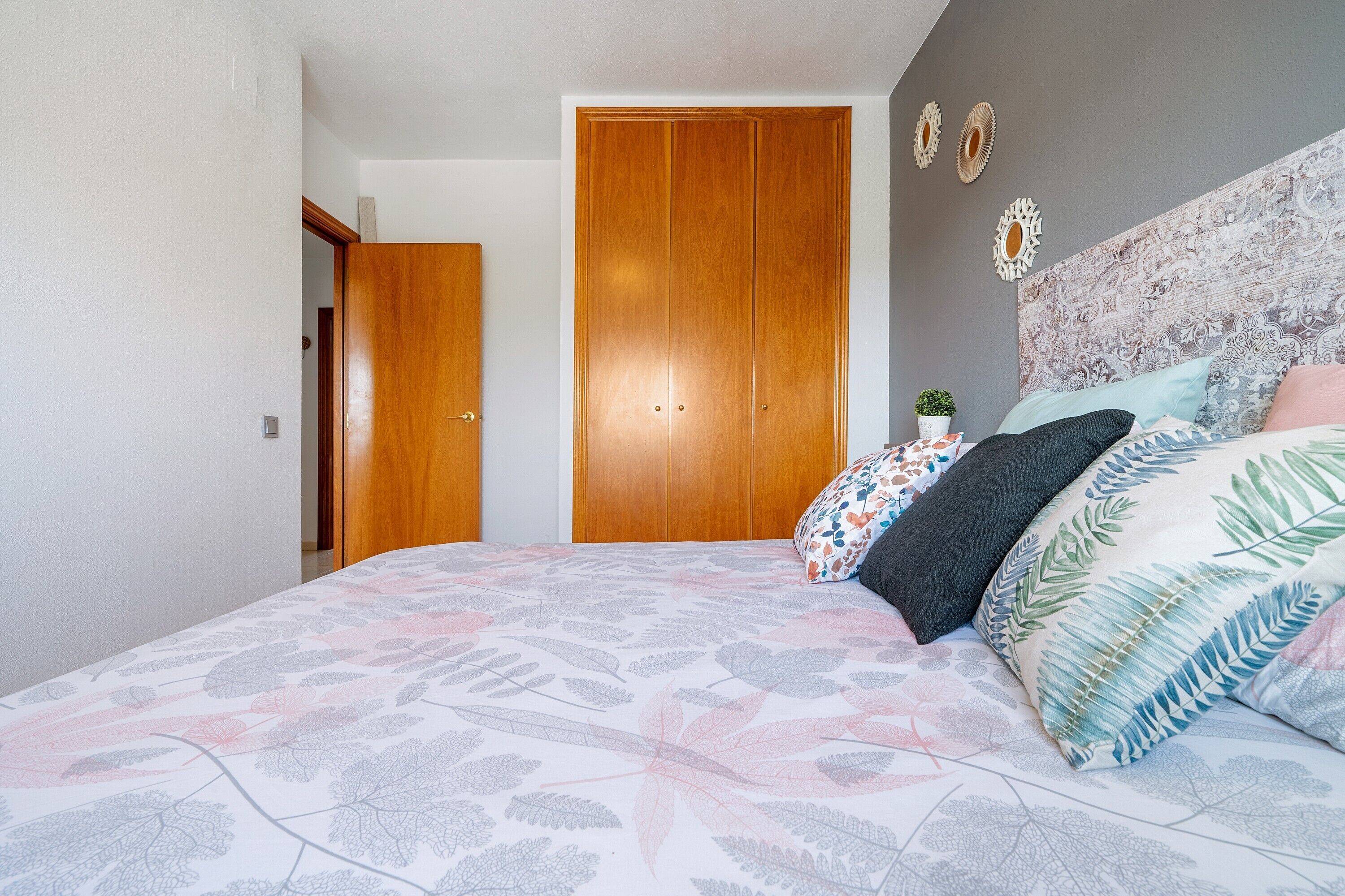 A bedroom with a bed, a wooden wardrobe, a small potted plant, and a wall with decorative items.