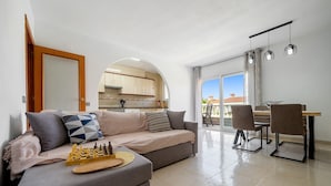 Una sala de estar con un sofá, un tablero de ajedrez y una zona de comedor con sillas y una mesa.