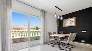 Una sala de estar moderna con comedor, grandes puertas de vidrio correderas a un balcón y una pared de acento negra con un cuadro enmarcado.