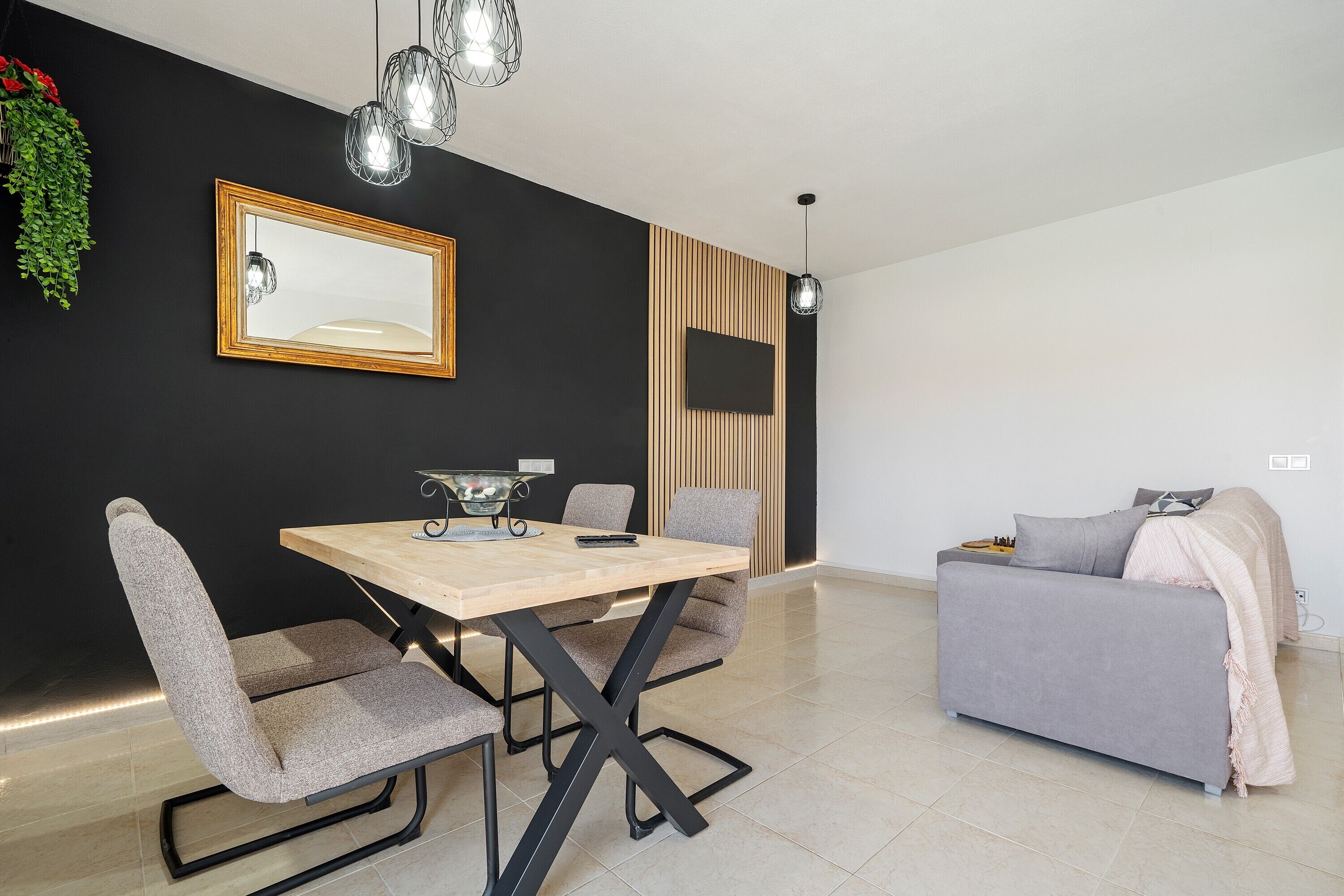 A modern living room with a dining table, chairs, a sofa, a TV, and a hanging plant.