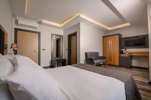 Una habitació d'hotel moderna amb un llit gran, una taula de treball, una cadira, un televisor i un armari.