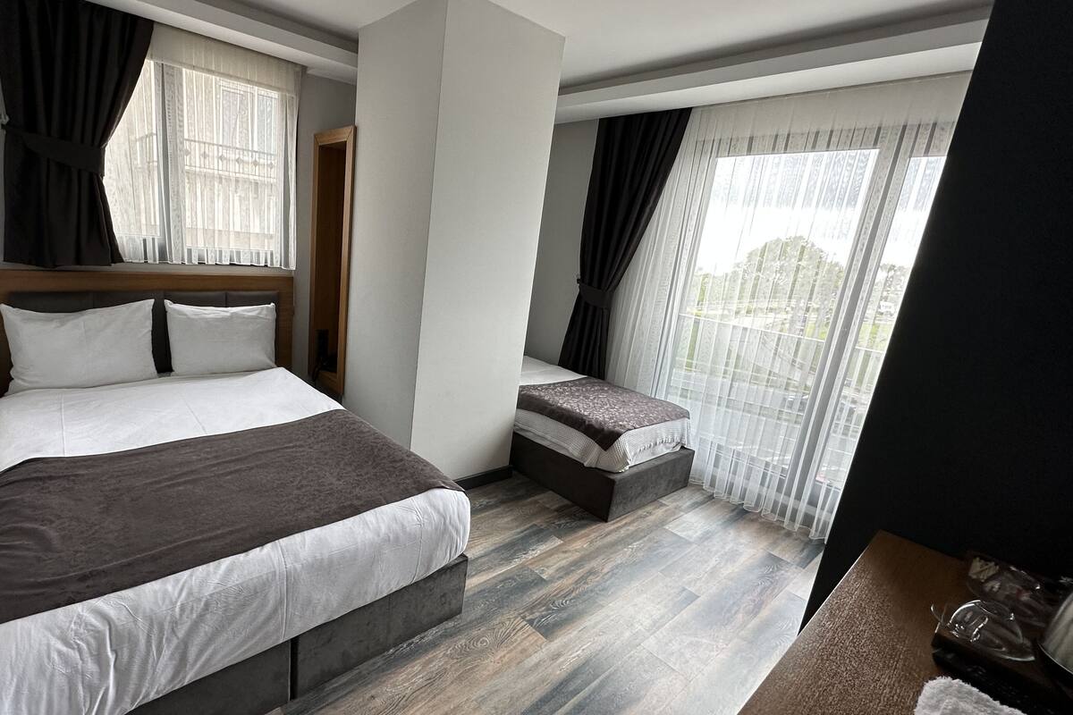 A modern bedroom with a large bed, a small bench, and a window with sheer curtains.