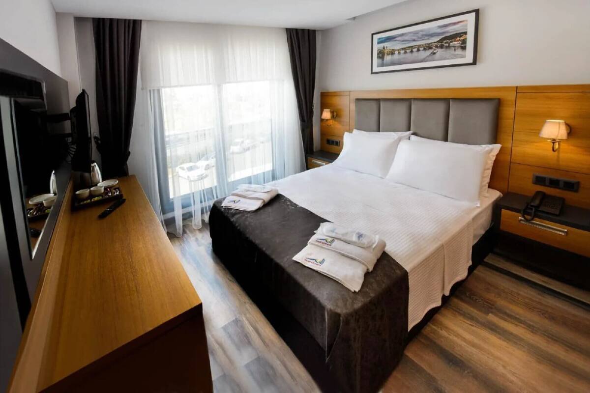 A hotel room with a large bed, a desk, a television, and a window with curtains.
