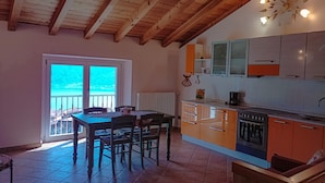 A kitchen with wooden beams, a dining area with chairs, a view through a glass door, and a kitchen counter with appliances. - Apartment 'Naol' with Lake View (tignale)