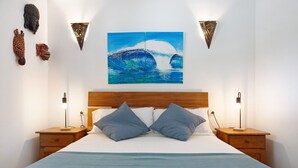 Un dormitorio con una cama, dos mesitas de noche, un cabecero de madera, un cuadro y luces fijadas a la pared.