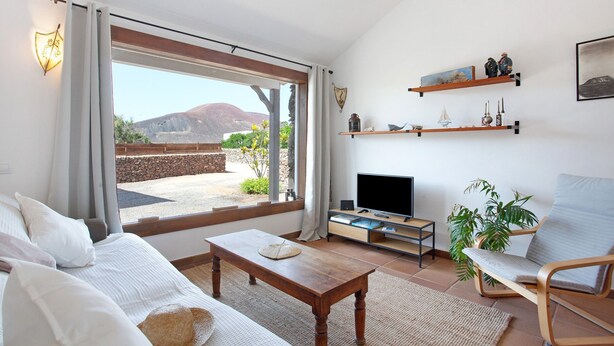 Una sala de estar con sofá, una mesa de centro, televisor y vistas a un paisaje montañoso a través de amplios ventanales.