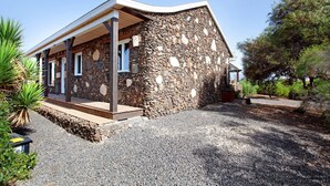 Un edificio de piedra con porche cubierto, camino de grava y vegetación circundante.