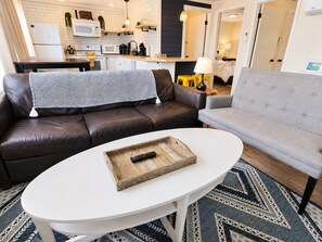 A living room with a brown leather sofa, a grey sofa, a white coffee table, and a kitchen in the background. - Tranquil Beach Retreat: Renovated 2nd Floor Apt Rehoboth Beach DE USA (Rehoboth Beach)