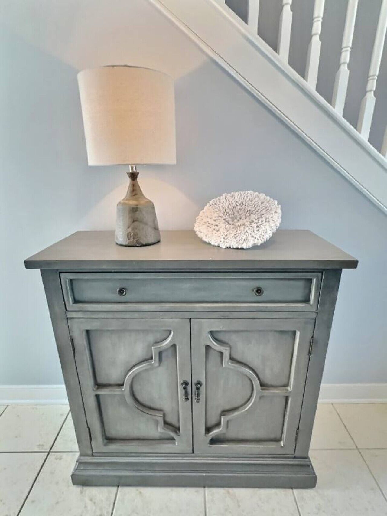A gray cabinet with two drawers and a lamp on top.