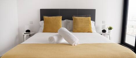 A neatly made bed with a rolled white towel, two mustard-colored pillows, and a mustard-colored bedspread.