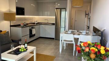 Una cocina moderna con armarios blancos, un refrigerador de acero inoxidable y un comedor con sillas blancas y una mesa dispuesta para cuatro.