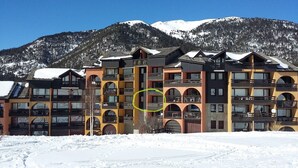 Un hotel de varios pisos con balcones, con una imponente montaña nevada de fondo.