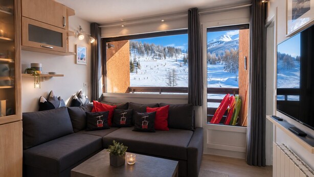 Una sala de estar moderna con un sofá modular, una mesa de centro con una planta y ventanas amplias que ofrecen vistas a un paisaje nevado.