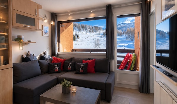 A modern living room with a sectional sofa, a coffee table with a plant, and large windows offering a view of a snowy landscape.