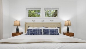 A neatly made bed with white bedding and two blue striped pillows, flanked by two bedside tables with lamps, in a room with white walls and a window above the bed. - Coastal Retreat, Close to the Beach (Pawleys Island)