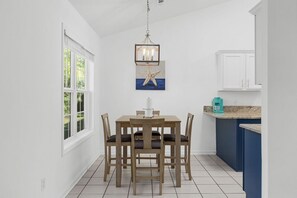 Ein Essbereich mit Holztisch und Stühlen, einer Kristallleuchter, einem Kunstwerk mit Seestern und einer Küche mit blauen Schränken.