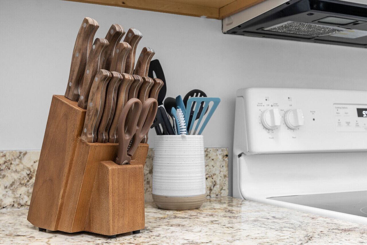 A kitchen with a wooden utensil holder containing knives and utensils, a white stove, and a marble countertop.