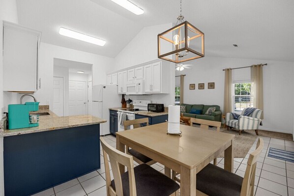 A modern kitchen with white cabinets, a central island, and a dining area with a wooden table and chairs.