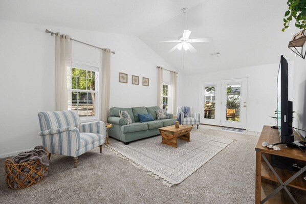 Ein geräumiges Wohnzimmer mit einem grünen Sofa, einem gestreiften Sessel und einem Holztisch.