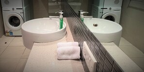 A bathroom with two sinks, a mirror, a towel rack, and a washing machine. - Darwin City Sea View Apartment with Balcony  (Darwin City)