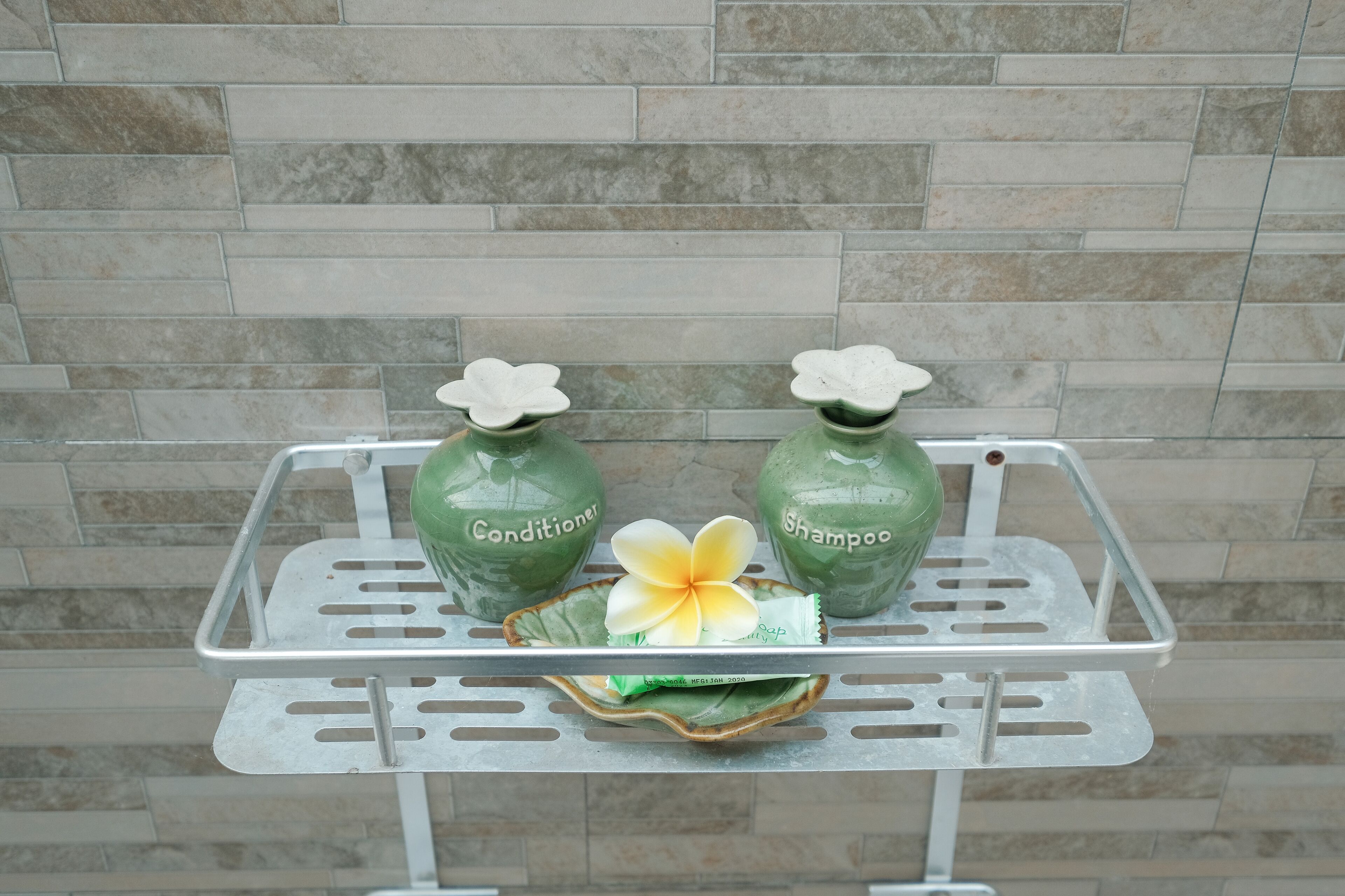 Ein Metallregal mit zwei grünen Flaschen, beschriftet mit 'Conditioner' und 'Shampoo', sowie einer dekorativen Blume.