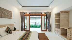 A bedroom with a large bed, a wooden wardrobe, and a view of a garden through open doors.
