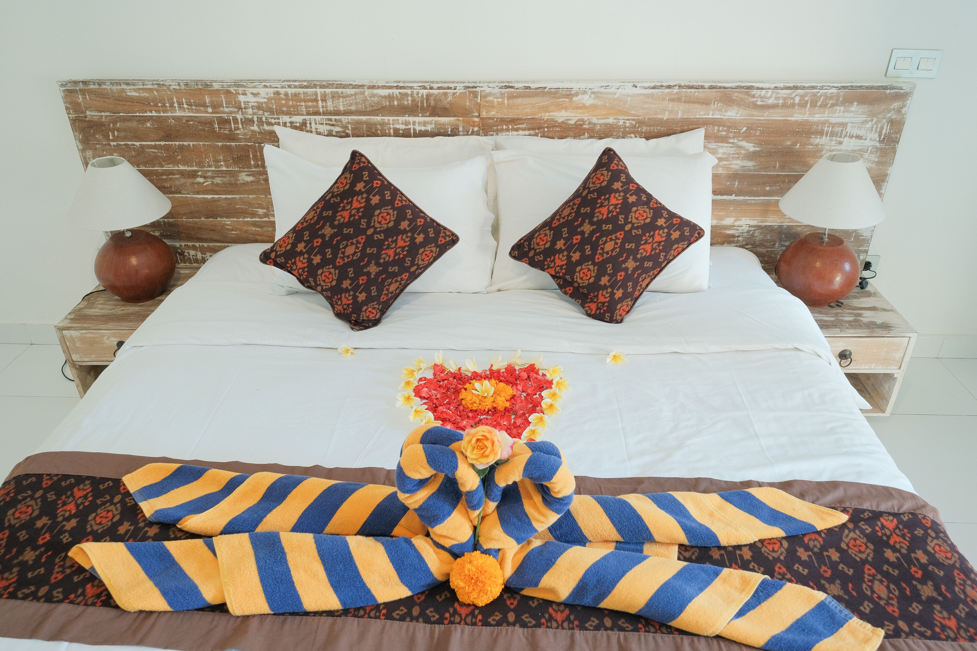 A neatly made bed with striped towels, two decorative pillows, and a flower arrangement.