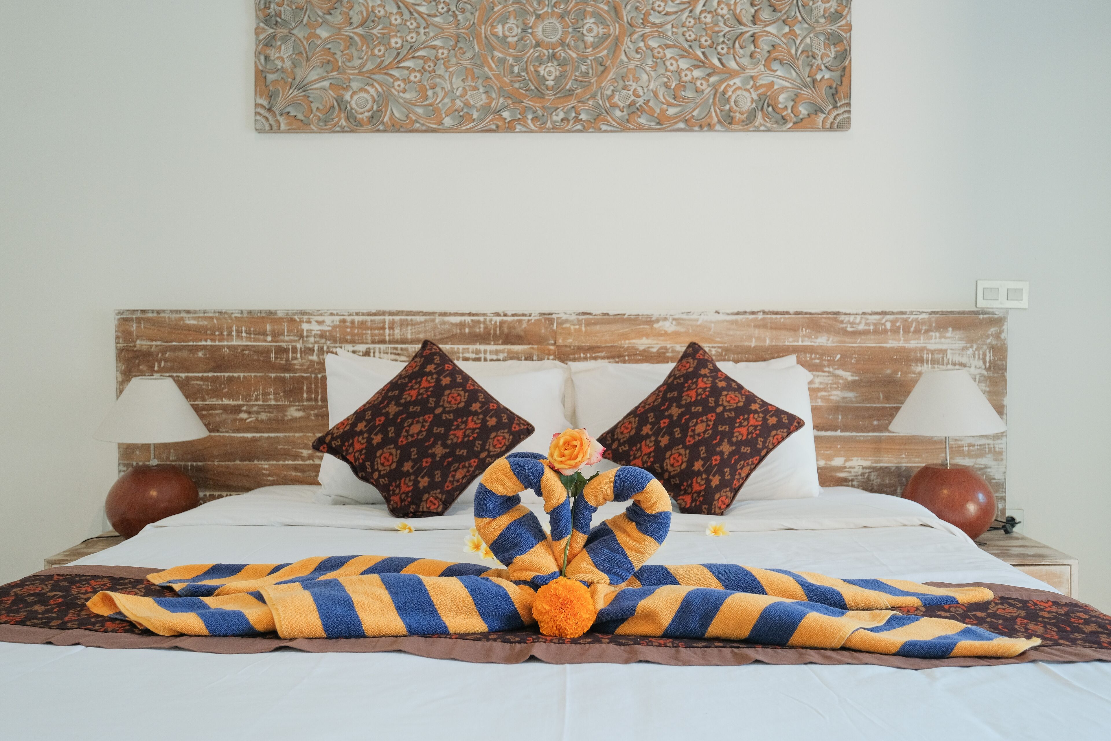 A neatly made bed with a striped blanket, two decorative pillows, and a single rose.