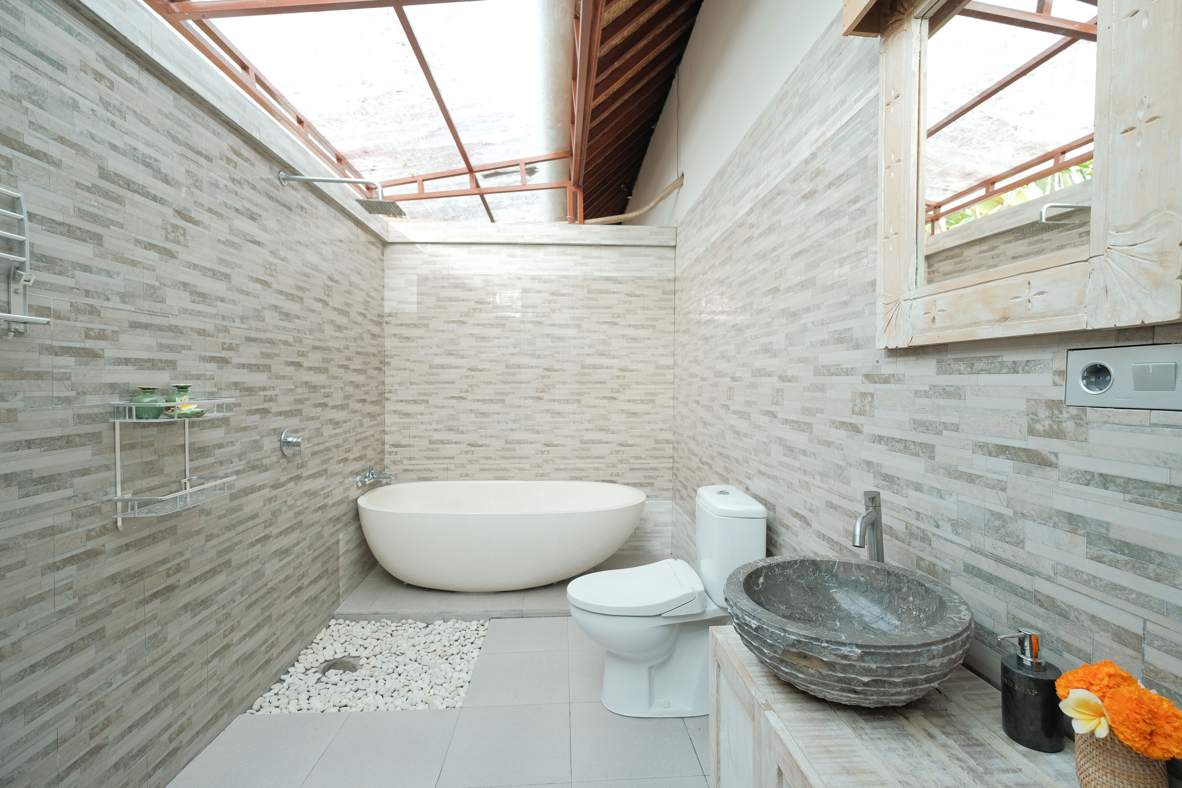 Un baño moderno con tragaluz, una bañera independiente, un inodoro y un lavabo de piedra.