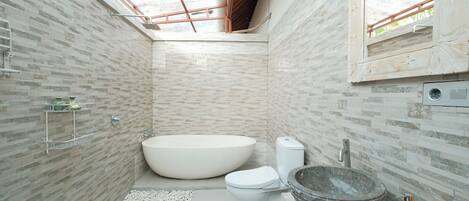 Un baño moderno con tragaluz, una bañera independiente, un inodoro y un lavabo de piedra.