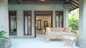 A spacious veranda with a cushioned sofa and a small table, surrounded by stone pillars and large windows.