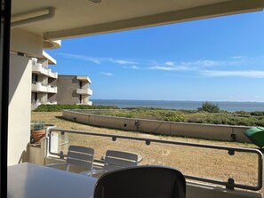 A balcony with a view of the sea, a building with balconies, and outdoor seating.